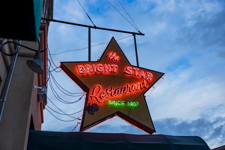 The iconic neon star sign for The Bright Star Restaurant in Bessemer, Alabama, glowing against a twilight sky. Established in 1907, this historic landmark is a staple of the Bessemer community.